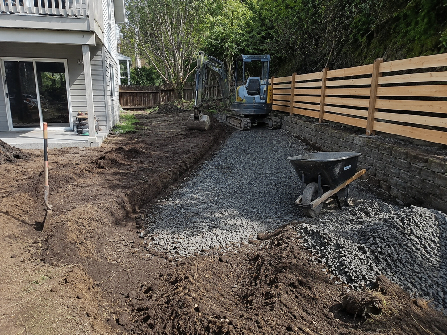 Excavation and gravel preparation beside a retaining wall and fence